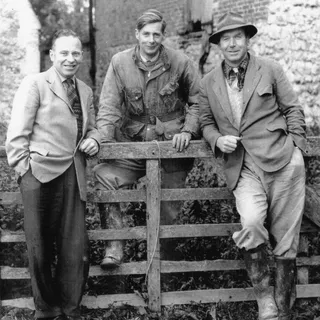 An old black-and-white family photograph of three farmers leaning on a fence